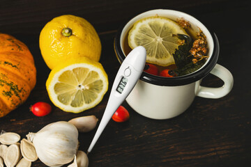 Cold and flu season and alternative medicine, natural remedies, digital thermometer, cup of herbal tea, lemon, garlic, pumpkin seeds and dog rose fruit on a dark wooden background