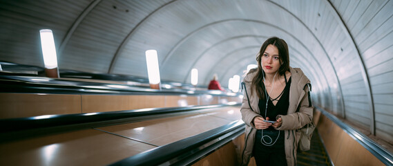 A young woman on an escalator in the subway with a phone in her hands.