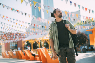 A young Caucasian man in an urban modern space. A handsome guy with a backpack walks around the city