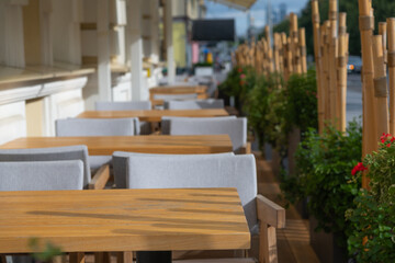 Close-up view of empty wooden tables of sidewalk cafe or street restaurant with bamboo fence in the morning. Focus on table surface. Copy space for your text or decoration. Food  business theme.