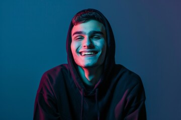 A joyful young man in a black hoodie radiates happiness in vibrant neon blue light against a dark background