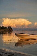 Small boat in front of a sunset sky reflecting in the sea. Colorful sky with almost no horizon. Stunning evening sky just after sunset. Yasawa Islands tranquility. Invisible horizon. Fiji.  