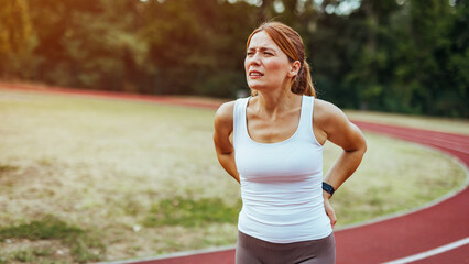 Back pain - woman having painful muscle injury in lower back. Back pain during sports. Young woman with an athletic figure and a lower back injury.