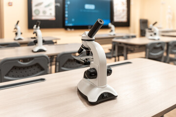 The microscope stands on a desk in the biology or natural science classroom, a school classroom. Selected focus