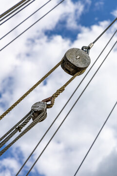 Old wooden pully on a ship with ropework against a blue summer sky