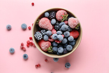 Bowl of different frozen berries on pink background