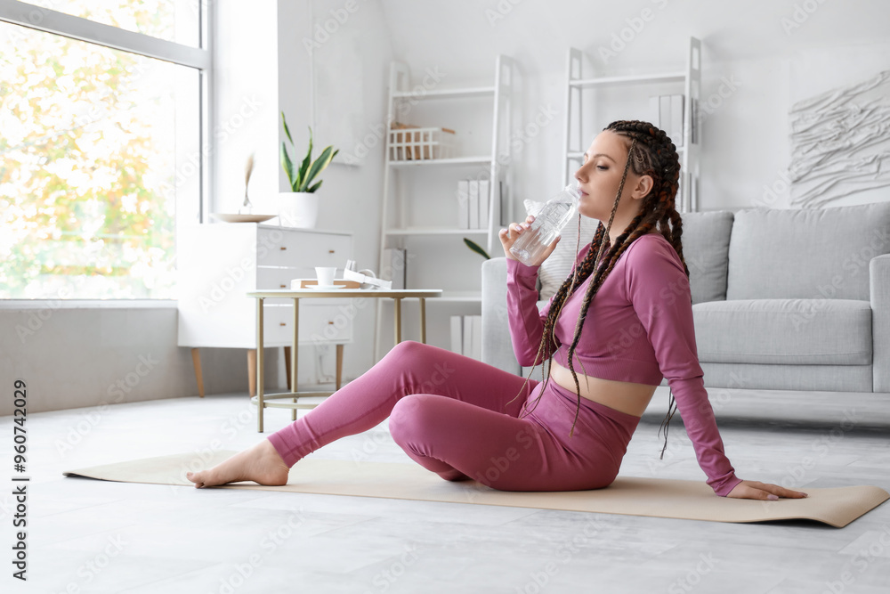 Poster young woman with dreadlocks drinking water after training at home