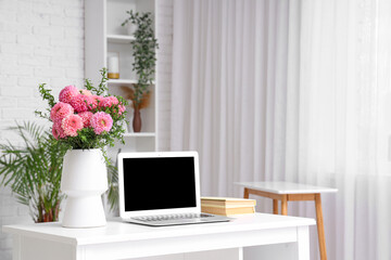 Vase of beautiful pink dahlias with books and laptop on table in living room