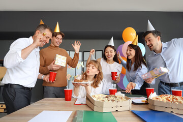 Young businesswoman with cake and her colleagues making wish at birthday party in office