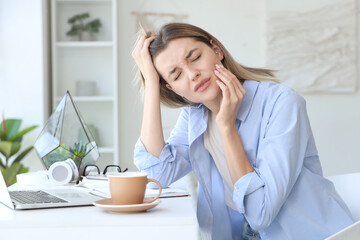 Young woman with laptop and cup of hot coffee suffering from tooth ache at home