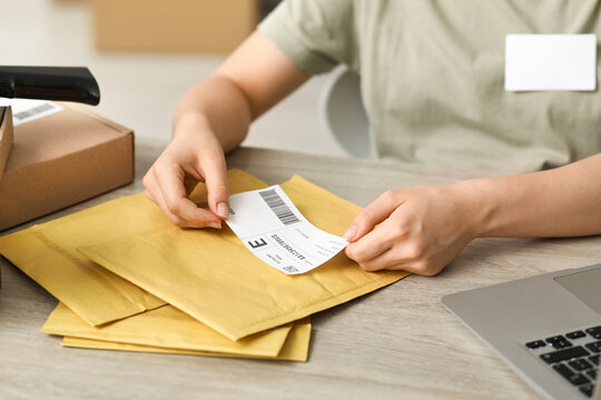 Female postal worker sticking label to package on table, closeup
