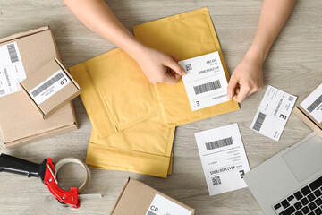 Female postal worker sticking label to package on table, top view