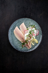 Traditional smoked rainbow trout with quark, radishes and pieces of cucumber served as top view on a designer plate