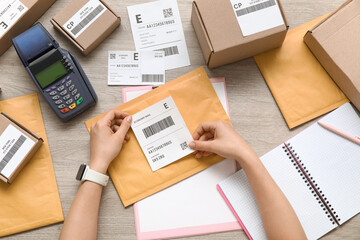 Female postal worker sticking label to package on table, top view