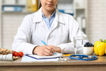 Young female nutritionist with glass of water and healthy food writing diet plan in office, closeup