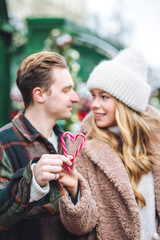 Obraz premium Beautiful young loving couple, boyfriend and girlfriend having fun on a christmas market wearing warm clothes. Outdoors, winter time, snowy weather. Tangerines in string bag, fir tree branches