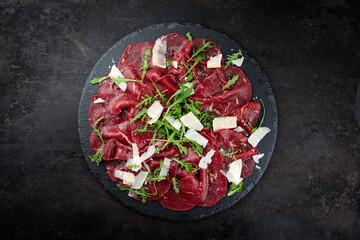 Traditional beef carpaccio served with parmesan and rocket salad as top view on a black design...