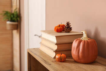 Different pumpkins with forest bump and books on commode near beige wall in stylish living room,...