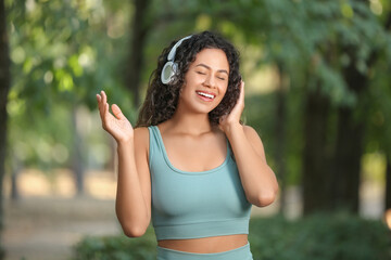 Sporty young African-American woman in headphones in park