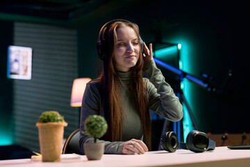 Cheerful gen Z girl filming herself listening to new album from favorite artist, reviewing music. Happy online star hosts internet show, rating songs, hearing them through headphones, feeling pleased