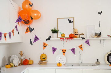 Interior of modern kitchen decorated for Halloween party with pumpkins, balloons and garlands