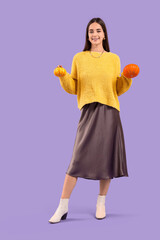 Beautiful young happy woman with pumpkins on purple background