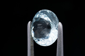 Close-Up of a Sparkling Blue Gemstone Held by Metal Tweezers on a Dark Background