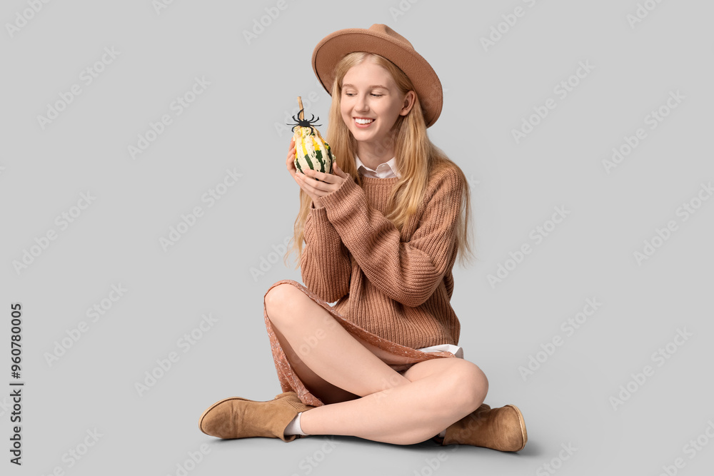 Poster beautiful young happy woman with halloween pumpkin and paper spider sitting on grey background