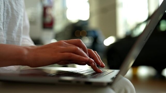 Focused female manager typing on laptop keyboard while seated in car dealership with modern interior, showcasing vehicles and creating professional atmosphere for business activities, closeup.