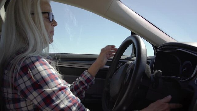 Old woman drive a car in hot and sunny day on highway. A woman with glasses is driving a car at deserts area during sunshine. Uber driver driving in beautiful place