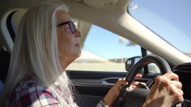 Old woman drive a car in hot and sunny day on highway. A woman with glasses is driving a car at deserts area during sunshine. Uber driver driving in beautiful place
