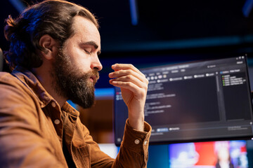 Stressed programmer shutting eyes to relax while fixing vulnerabilities in software systems. Tired...