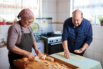 Senior latin couple preparing fresh chilean fried biscuits calzones rotos, sweet pastry in domestic kitchen