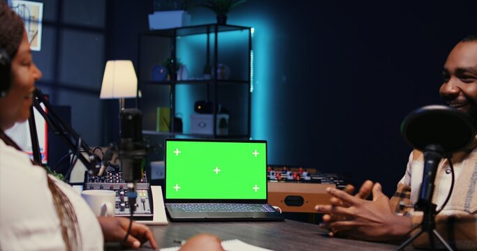 Isolated screen laptop next to cohosts streaming podcast using professional vlogging gadgets on internet channel. Chroma key notebook between man and woman meeting in studio to film online show