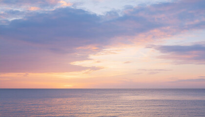 Fototapeta premium Sunset paints the sky with vibrant hues of pink, purple, and golden light, reflecting on the calm waters of the ocean. 