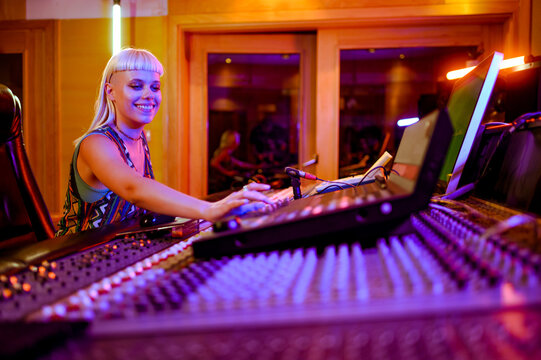 Blonde woman sound engineer working at the soundboard in her music studio