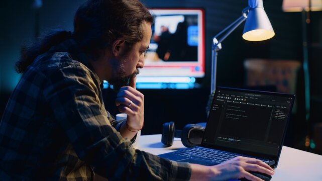 Experienced programmer writes code on laptop screen while in apartment office using Java programming languages. Developer remotely working on fixing database errors while working from home, camera A