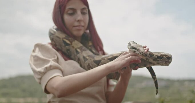 A young red-haired woman gently holds a large snake in her arms, showcasing a connection with nature and reptiles.