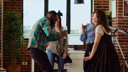 Diverse group of school colleagues organizing apartment party, enthusiastically dancing to electronic songs. Friends enjoying time spent together, busting into animated dance moves in cozy house