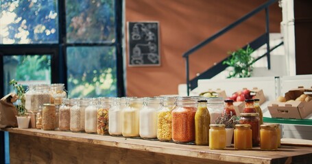 Pasta and sauces in reusable glass jars on store shelves, low carbon footprint sustainable lifestyle organic shop. Empty farmers market filled with bulk products and fresh produce. Handheld shot.