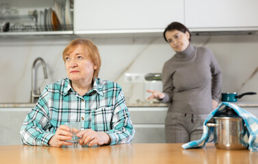 Obraz premium Frustrated mature woman sitting at a table in a home kitchen after a conflict with her daughter
