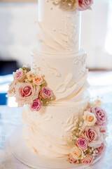 White luxury cake decorated with pink roses. Beautiful multi-tiered wedding cake stands on the table in the restaurant. Traditional wedding cake for the bride and groom. Close-up cake-shaped pastries