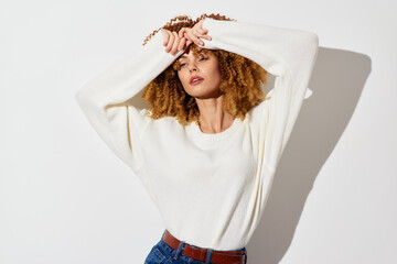 Casual fashion portrait of a woman in a white sweater with curly hair against a neutral light...