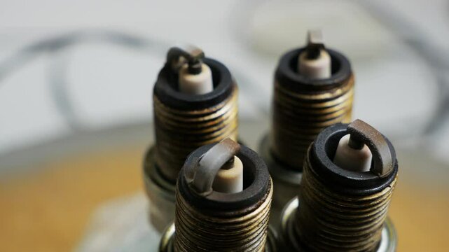Mechanic rotates a set of four used spark plugs on a table, closely examining their condition and assessing wear, dirt, and potential issues for engine performance