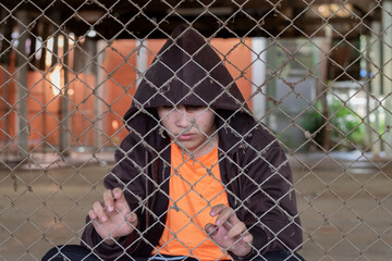 Asian teenager puts his hand on the metal fence around his house because he was detained for inappropriate behavior, freedom, social problems, drug addiction and detention of young people  concept.