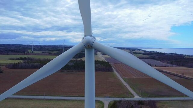 Face a face avec un rotor d'&eacute;olienne en rotation avec en arri&egrave;re-plan des champs cultiv&eacute;s, un chemin et des bandes foresti&egrave;res sous un ciel nuageux ( Parc &eacute;olien de Baie-des-Sables, Qu&eacute;bec )