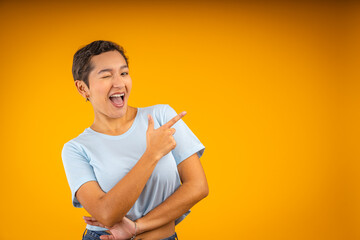 Young woman winking and pointing with finger on yellow background