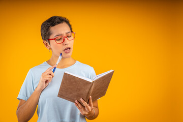 Young woman thinking with pen and notebook in hand on yellow background