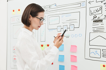 Developing UI design. Woman drawing website wireframe on whiteboard indoors