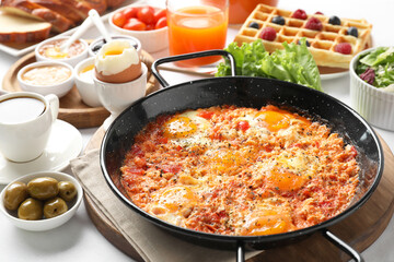 Tasty shakshouka in frying pan and other meals served for breakfast on white table, closeup